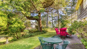 Une terrasse avec une table et des chaises, entourée de verdure et d’arbres.