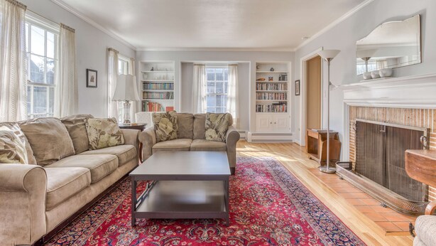 Un salon comprenant un canapé, une table basse, une cheminée, des étagères et un tapis à motifs.