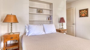 Une chambre à coucher avec un lit, une table de chevet, une étagère et une porte.