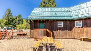 A rustic wooden building with a green metal roof, a wooden bench, and a paved patio area. - 2-story dog-friendly cabin near White Salmon River with mtn views, courtyard, AC (White Salmon)