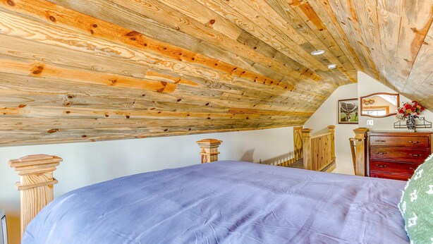 A bedroom with a sloped ceiling, wooden beams, a bed with a blue bedspread, a dresser, and a small decorative item on the dresser. - 2-story dog-friendly cabin near White Salmon River with mtn views, courtyard, AC (White Salmon)