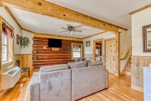 Ein Holzblockhaus-Innenraum mit einer Couch, Holzwänden, einem Deckenventilator und einer Treppe.