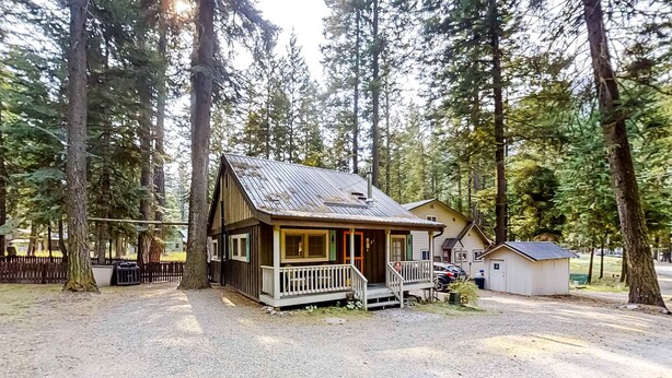 Eine Hütte mit Veranda, umgeben von hohen Bäumen, und ein kleines Nebengebäude.