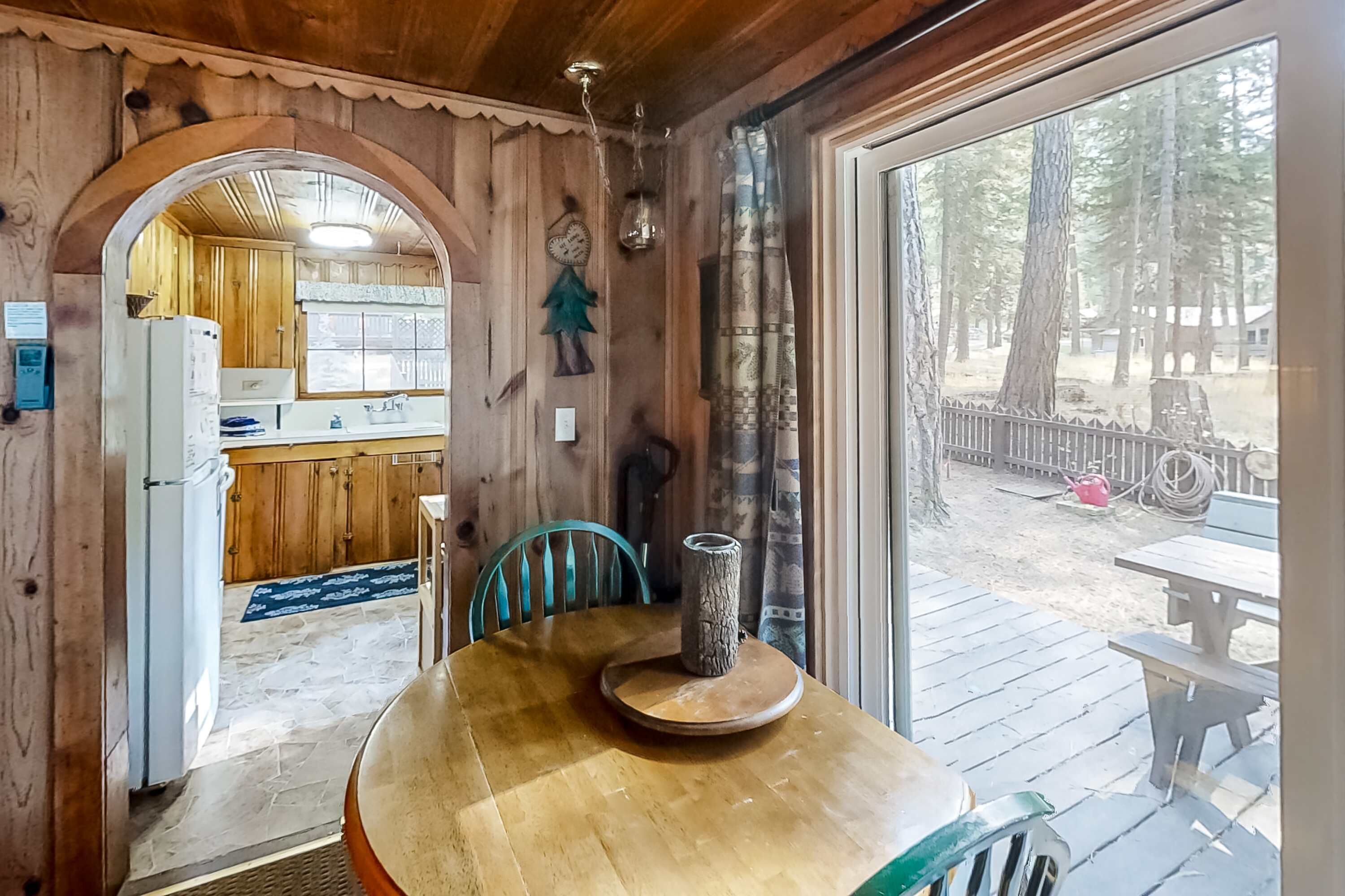 A wooden interior with a dining table, chairs, a view of the outdoors, and a kitchen area.