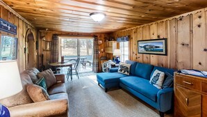 Ein Interieur mit Holzbalkendecke, einem blauen Sofa, einem Holzschrank und einem Esstisch mit Stühlen.