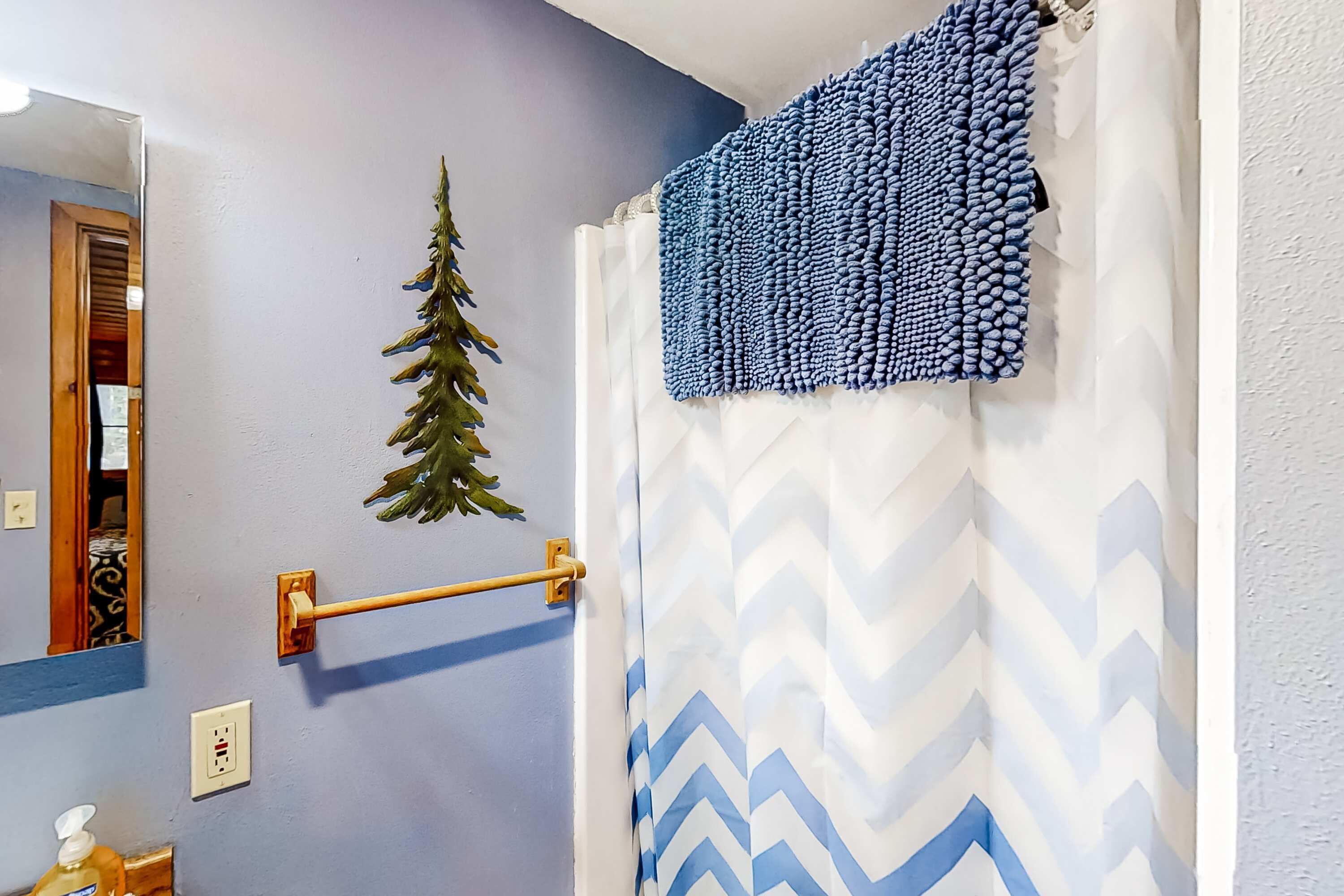 A bathroom with a mirror, a towel rack, a soap dispenser, a decorative pine tree, and a shower curtain with a chevron pattern.