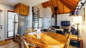 Un coin repas avec une table et des chaises en bois, une cuisine équipée d’un réfrigérateur et d’une cuisinière, un escalier et un téléviseur dans l’espace de vie.