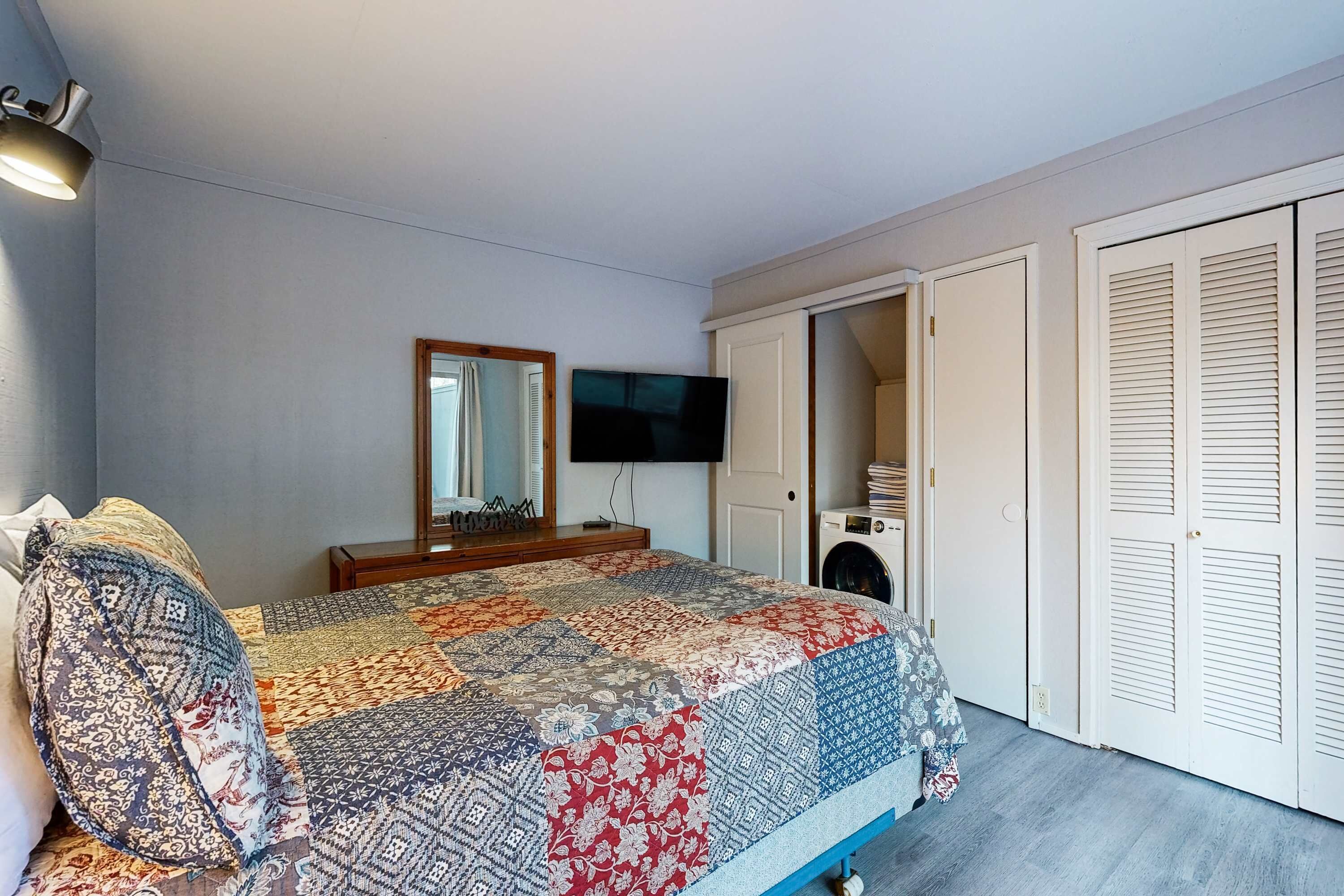 A bedroom with a bed, a television, a mirror, and a wardrobe.