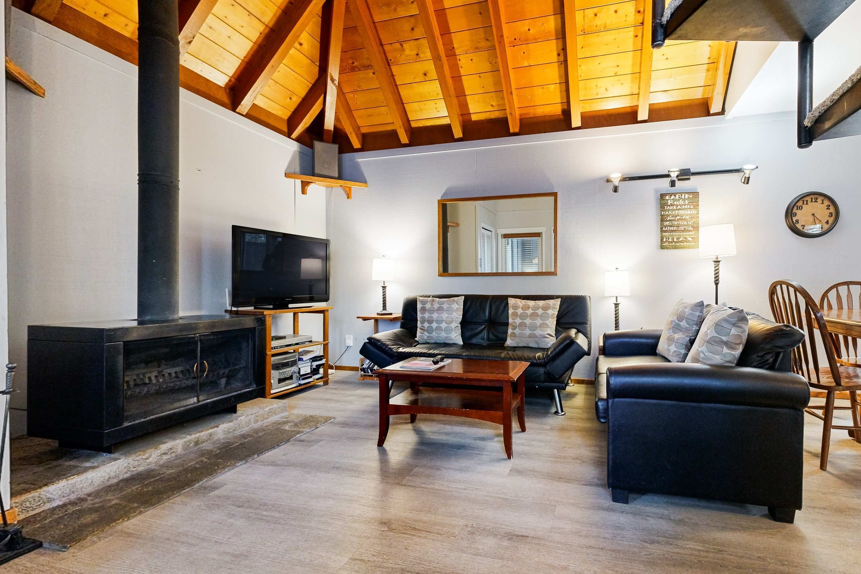 Uma sala de estar com lareira, sofá, televisão e vigas de madeira no teto.