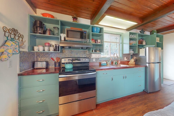 A kitchen with teal cabinetry, stainless steel appliances, and a wooden floor.