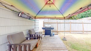 An outdoor patio with a wooden deck, a grill, and a covered seating area with chairs and a table.