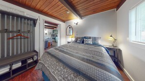 A bedroom with a wooden ceiling, a bed with patterned bedding, a bedside lamp, and a window with blinds.