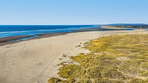 Een kustlandschap met een zandstrand, begroeide duinen en een heldere blauwe lucht.