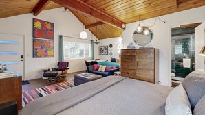 Een slaapkamer met een groot bed, een houten plafond, een bureau, een stoel, een bank en kunstwerken aan de muur.