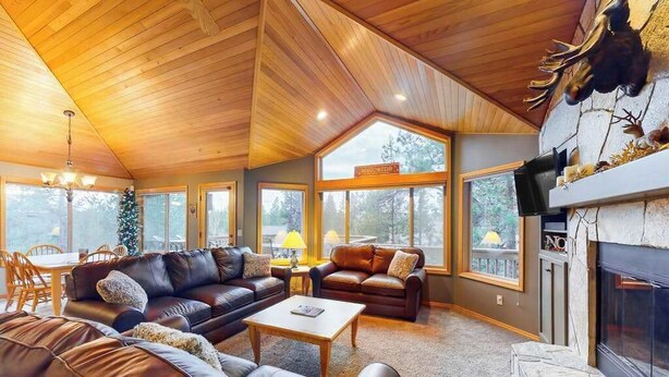 A spacious living room with leather sofas, a fireplace, and large windows offering a view of the outdoors. - Inviting house with hot tub, game tables, bikes, & partial mountain view (Sunriver)