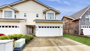 Un immeuble résidentiel de deux étages, doté d’un garage, d’une porte d’entrée et d’un petit jardin devant, avec une pelouse et un pot de fleurs.