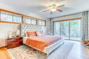 A bedroom with a large bed, a ceiling fan, a nightstand, a dresser, and a window with blinds.