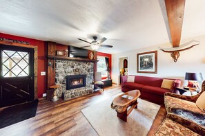 Interior d'una cabana amb una llar de pedra, un sofà vermell, una taula de centre de fusta i un ventilador de sostre.