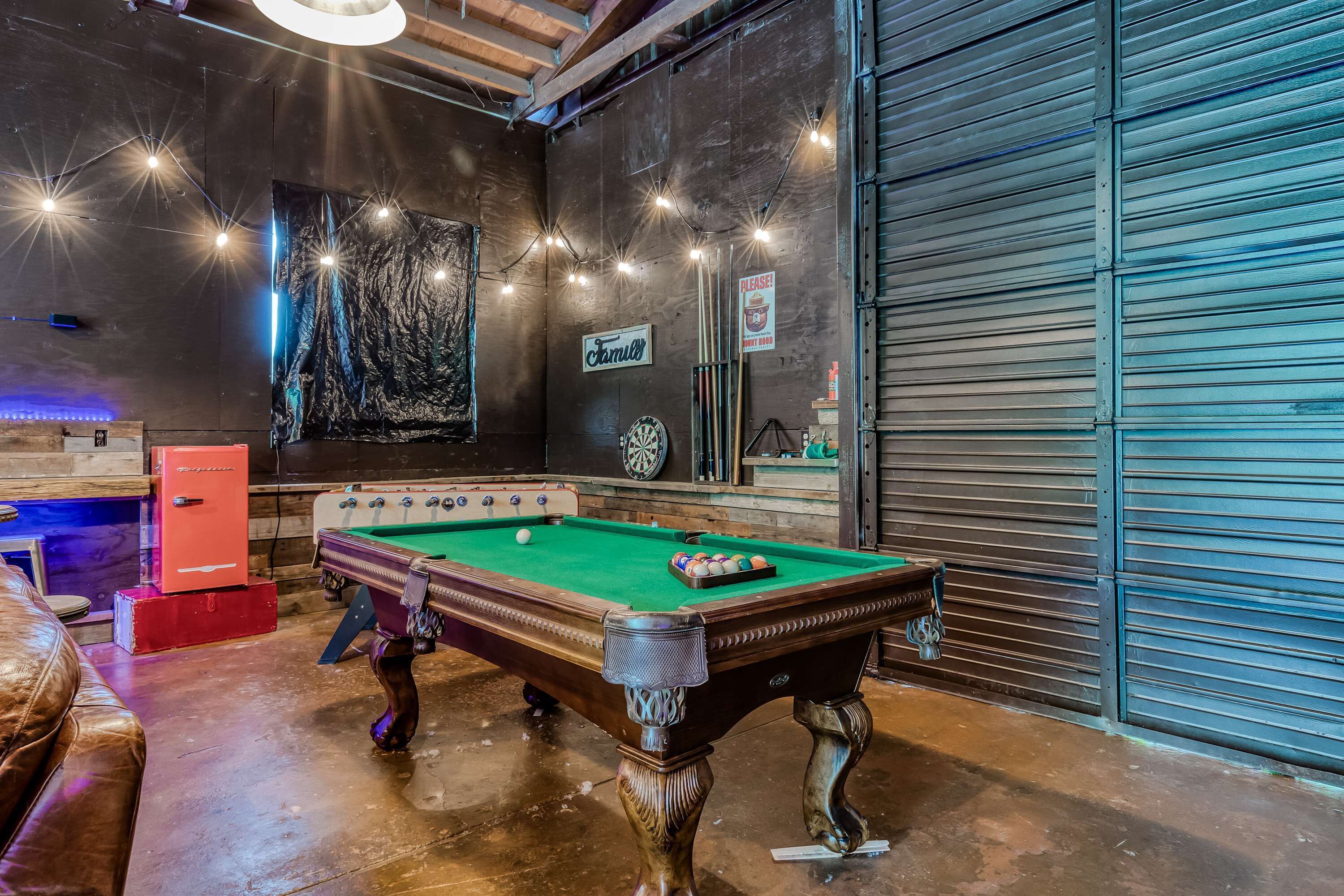 Een pooltafel in een ruimte met een dartbord, een bord waarop 'Farnsworth' staat en een gesloten garage deur.