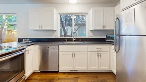 A modern kitchen with white cabinets, stainless steel appliances, a dishwasher, and a window above the sink. - Beautiful home with patio - in the perfect location near Downtown Bend & more (Bend)