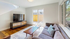 A modern living room with a flat-screen TV, a sofa, a coffee table, and a sliding glass door leading to an outdoor area. - Beautiful home with patio - in the perfect location near Downtown Bend & more (Bend)