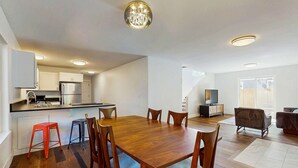 A modern kitchen with white cabinets, a wooden dining table, and a chandelier. - Beautiful home with patio - in the perfect location near Downtown Bend & more (Bend)