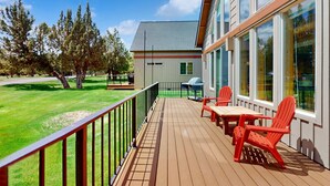 Une terrasse en bois, dotée de mobilier d’extérieur et d’une rambarde en métal, et offrant une vue sur un immeuble aux grandes fenêtres.