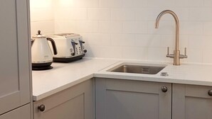 Une cuisine compacte comprenant un évier, des placards blancs, un plan de travail et une bouilloire.