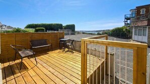 A wooden deck with outdoor furniture, a view of the street, and a fence. - Perfect Family Base: Spacious Seaside Apartment with Parking (Swanage)