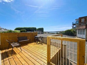 A wooden deck with outdoor furniture, a view of the street, and a fence.