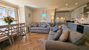 A modern living room with a sofa set, a dining table with chairs, and a kitchen area with cabinets and appliances. - Perfect Family Base: Spacious Seaside Apartment with Parking (Swanage)