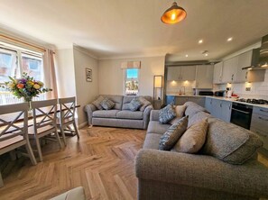 A modern living room with a sofa set, a dining table with chairs, and a kitchen area with cabinets and appliances.