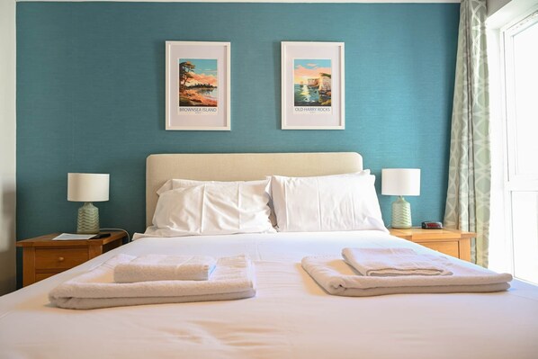 A hotel room with a bed, two framed pictures on the wall, two bedside lamps, and a window with curtains.