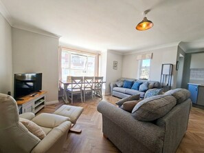 Una sala de estar con un sofá, un televisor y una zona de comedor con una mesa y sillas.