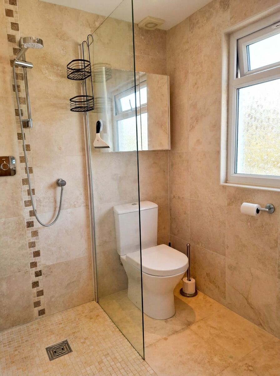 A bathroom with a glass-enclosed shower, a toilet, and a window.