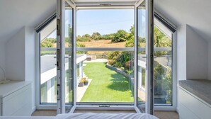 A bedroom with a large skylight and a view of a green lawn and trees. - Spacious Countryside Home with Games Room & Large Garden Near Swanage (Langton Matravers)