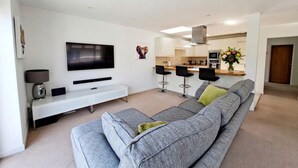 A modern living room with a grey sofa, a flat-screen TV, and a minimalist design. - Spacious Countryside Home with Games Room & Large Garden Near Swanage (Langton Matravers)