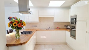 A modern kitchen with white cabinets, a wooden countertop, a gas stove, an oven, and a stainless steel range hood. - Spacious Countryside Home with Games Room & Large Garden Near Swanage (Langton Matravers)