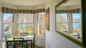 A dining area with a bay window, a table, chairs, and a large mirror.