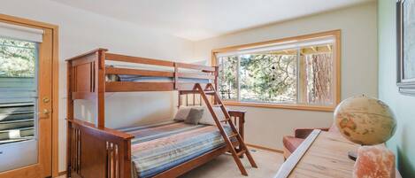 A bunk bed with a ladder, a desk with a globe and a salt lamp, and a window with a view of trees.