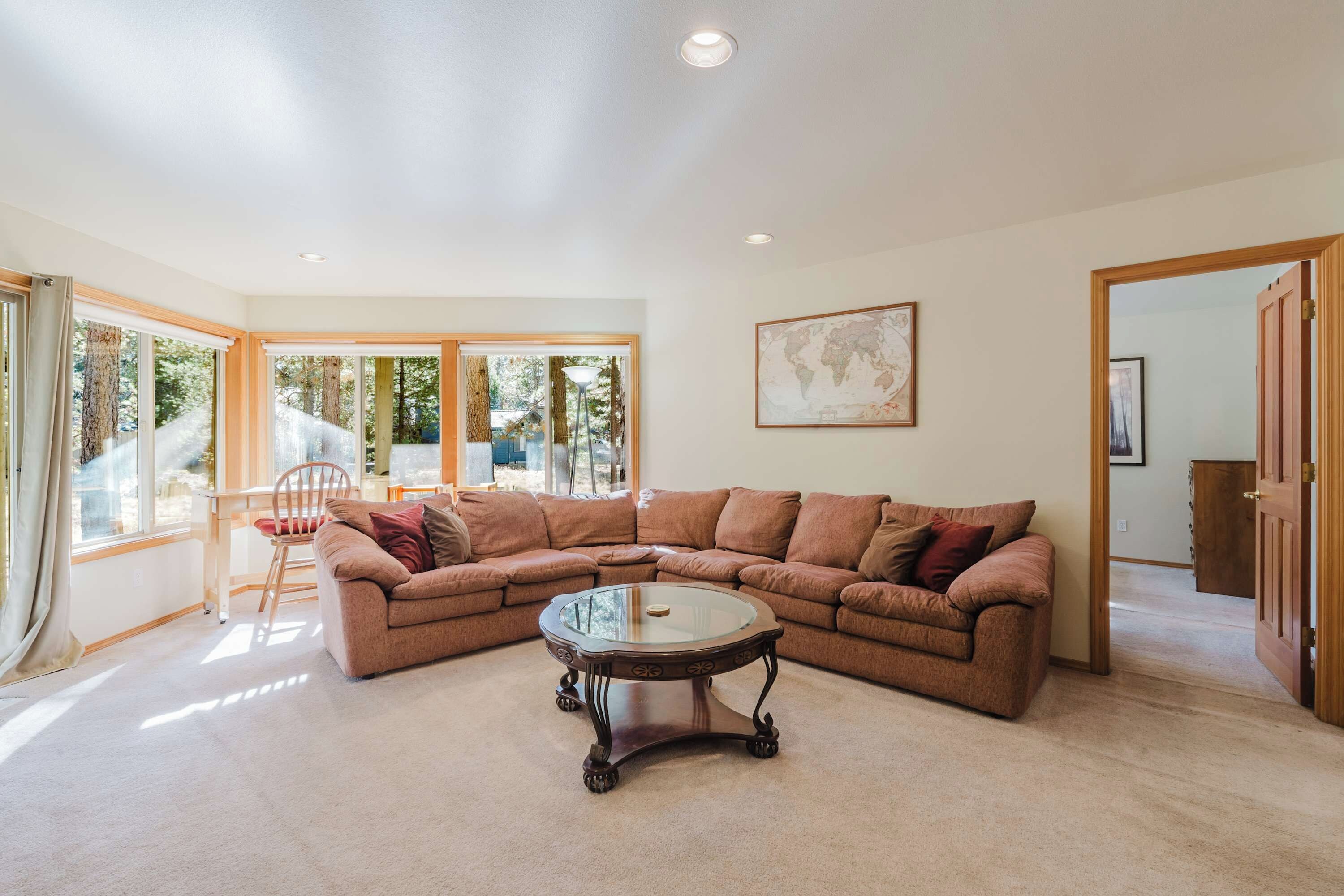 A spacious living room with a large sectional sofa, a glass coffee table, and a world map on the wall.