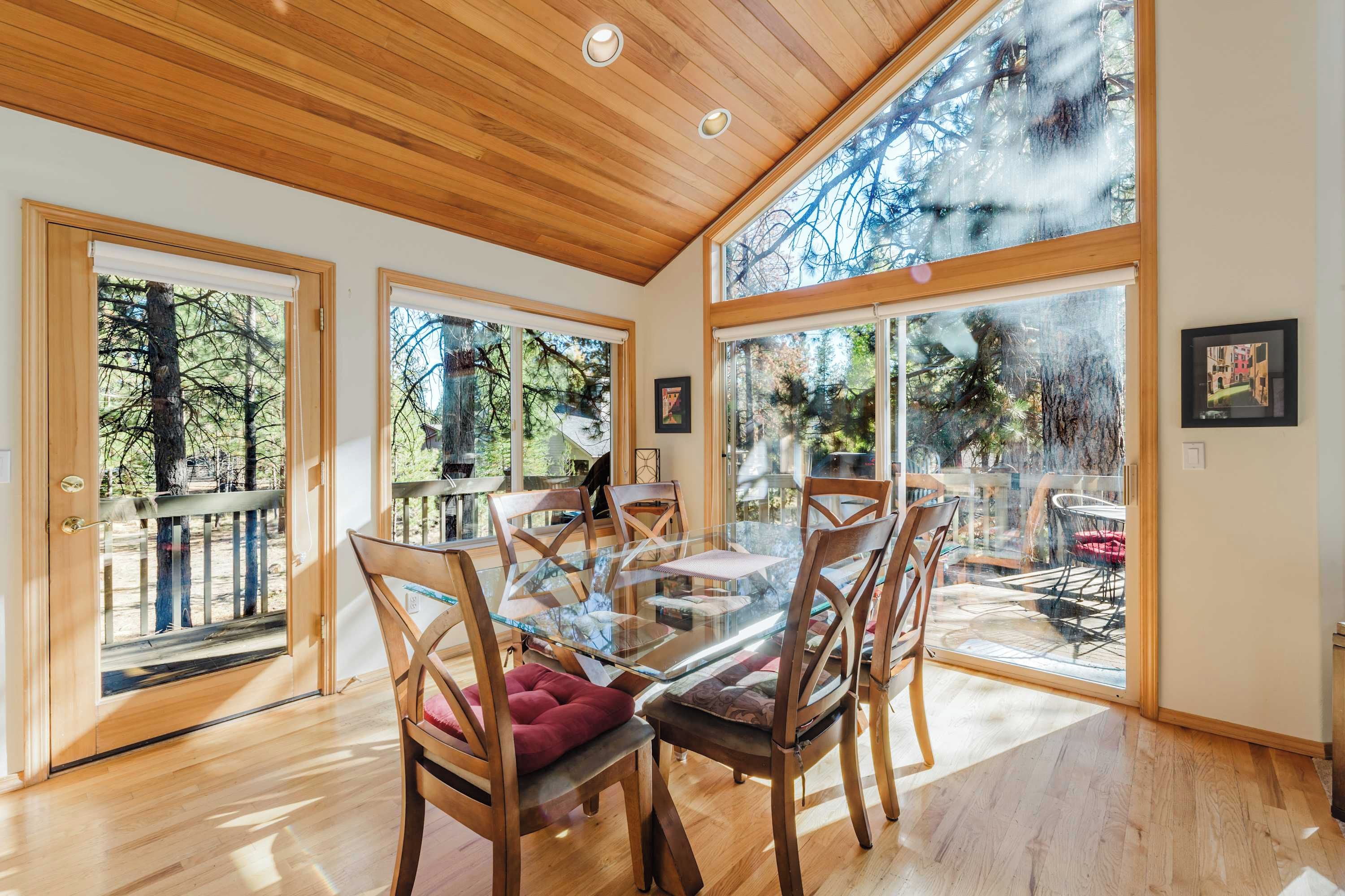 A spacious room with a wooden ceiling, large windows, and a glass dining table with chairs.