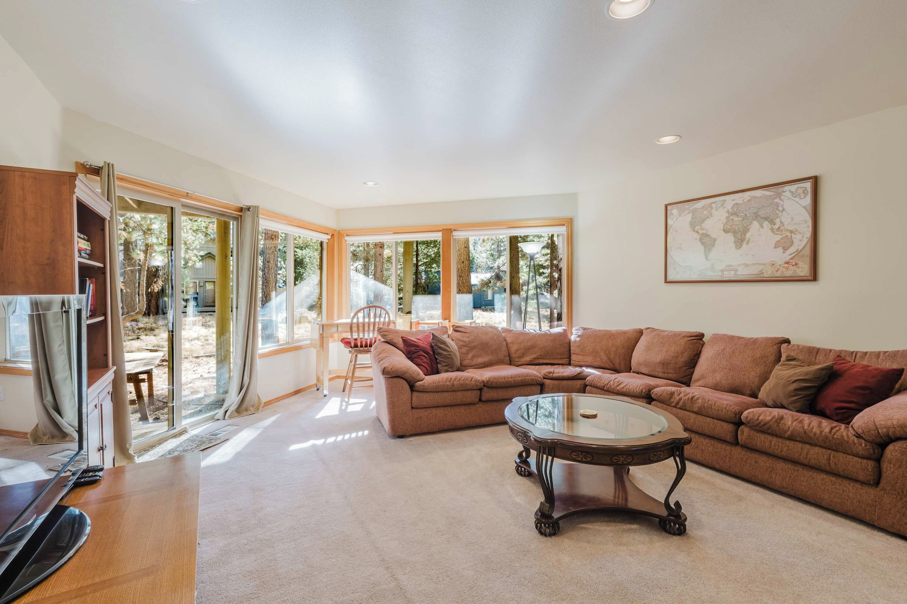 A spacious living room with a large sectional sofa, a glass coffee table, and a world map on the wall.