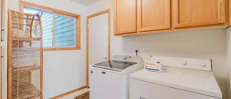 A laundry room with a washing machine, dryer, wooden cabinets, a window, and a wicker basket.