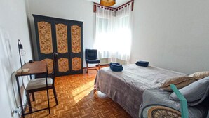 Een slaapkamer met een bed, een stoel, een bureau, een kledingkast en een raam met gordijnen.