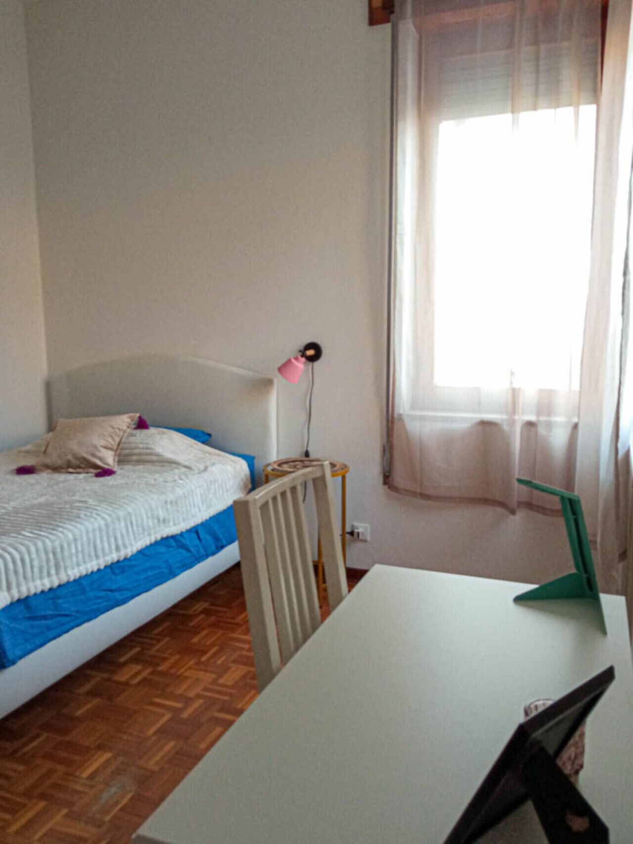 Une chambre à coucher avec un lit, un bureau, une chaise, une lampe et une fenêtre avec des rideaux.