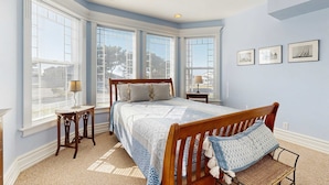 A bedroom with a large bed, a nightstand, a chair, and a window with blinds. - Side-by-side ocean view homes with enclosed yard & hot tubs - 1 block to beach (Newport)