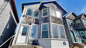 A multi-story residential building with a prominent bay window, a front door with a glass panel, and a small blue pot on the steps. - Side-by-side ocean view homes with enclosed yard & hot tubs - 1 block to beach (Newport)