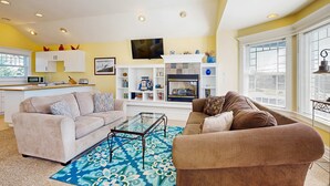 A living room with two sofas, a coffee table, a fireplace, and a TV mounted above it. - Side-by-side ocean view homes with enclosed yard & hot tubs - 1 block to beach (Newport)