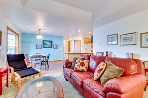 A living room with a red leather sofa, a glass coffee table, and a dining area with a wooden table and chairs. - Dog-Friendly Home with Private Hot Tub - Near City Park and Beach Access (Seaside)